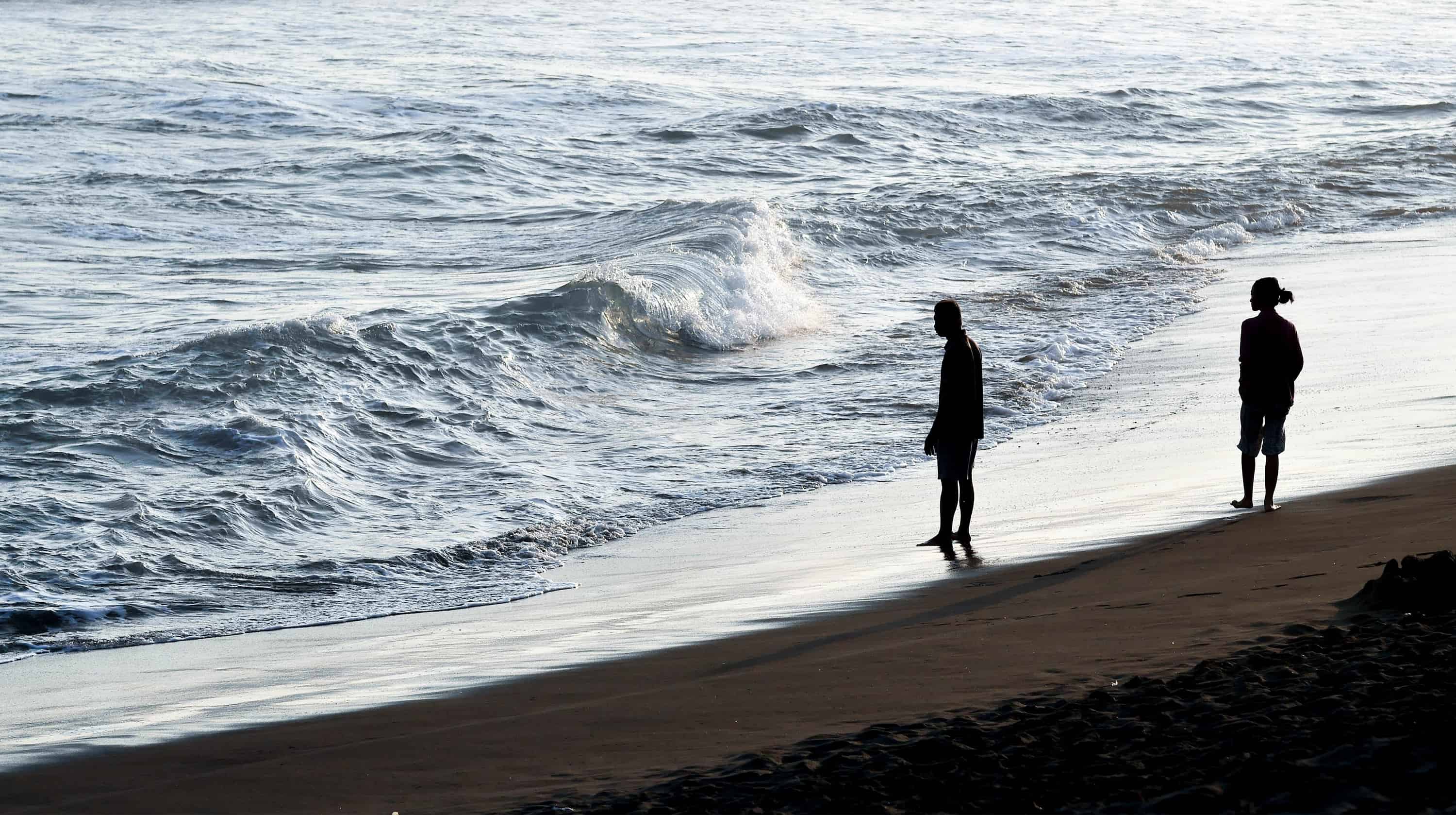 A couple walks apart from each other at sunset on the beach.