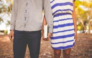 Close up of young couple holding hands which are also holding a Bible together. The couple's heads are not shown.