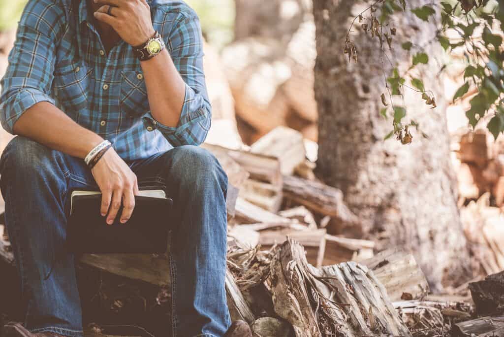 Man sitting on log holding Bible and thinking