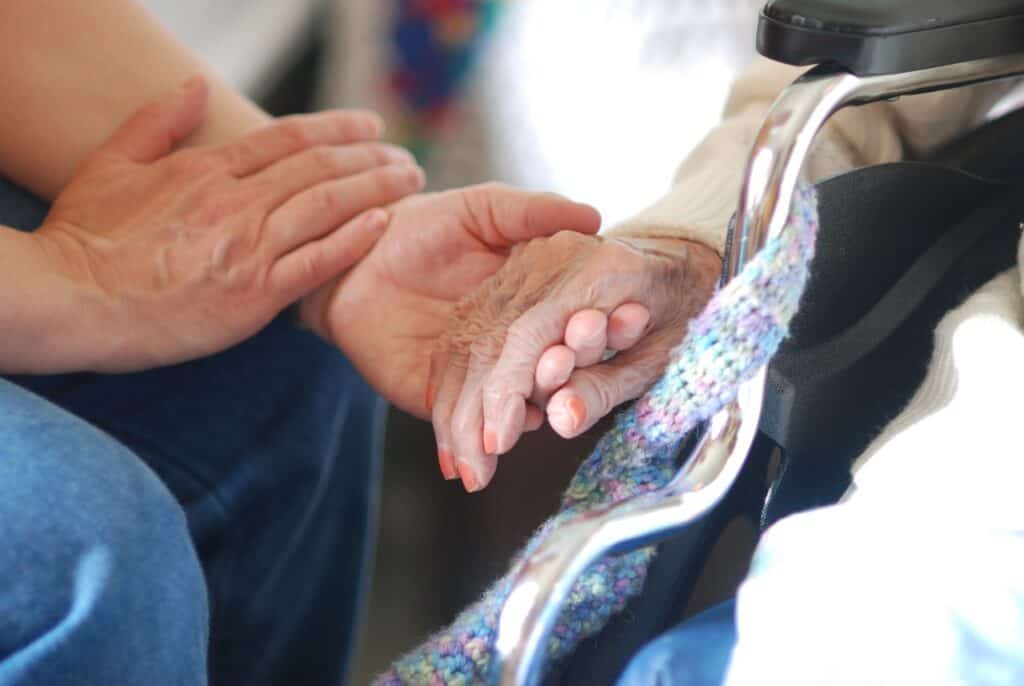 younger hands holding elderly woman hand