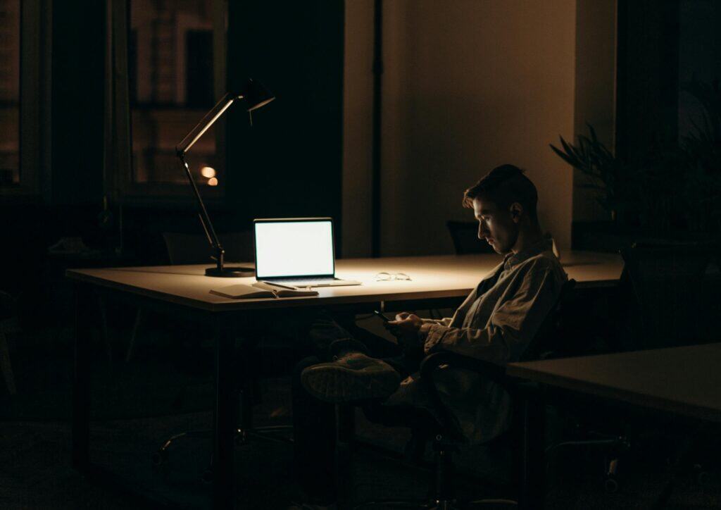 man in dark on computer and phone