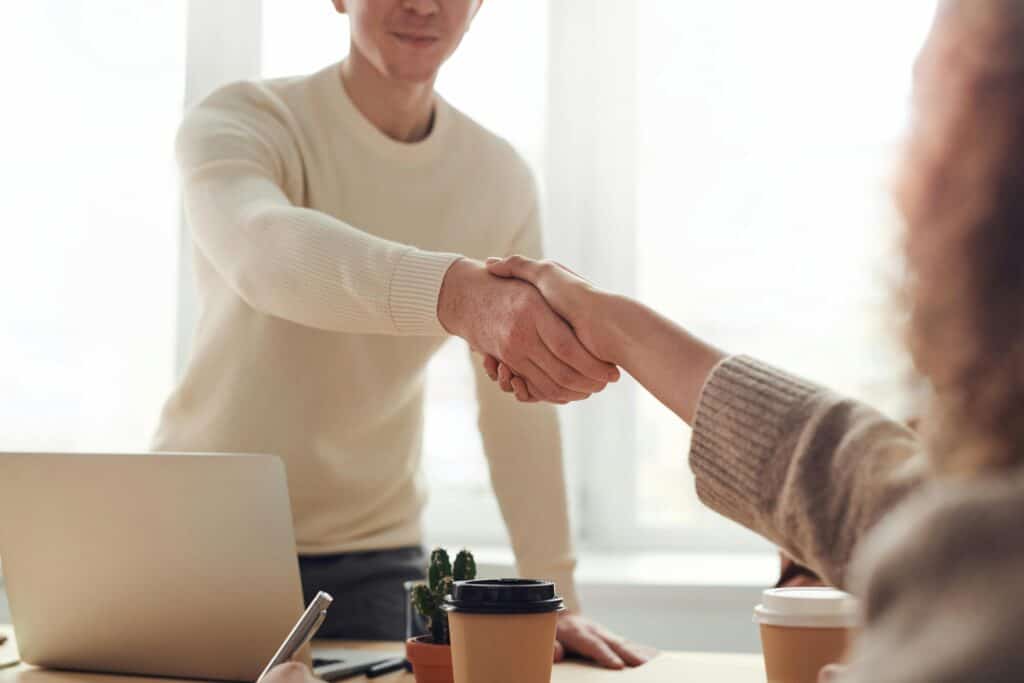 man and woman shaking hands over desk coffee computer