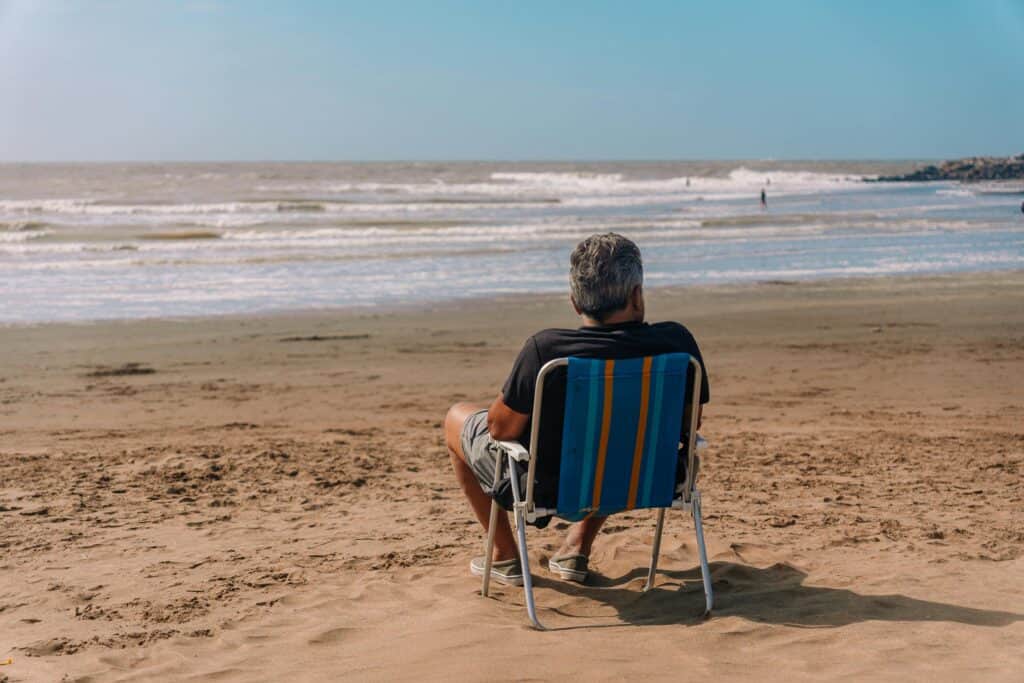 back of man sitting in chair on beach
