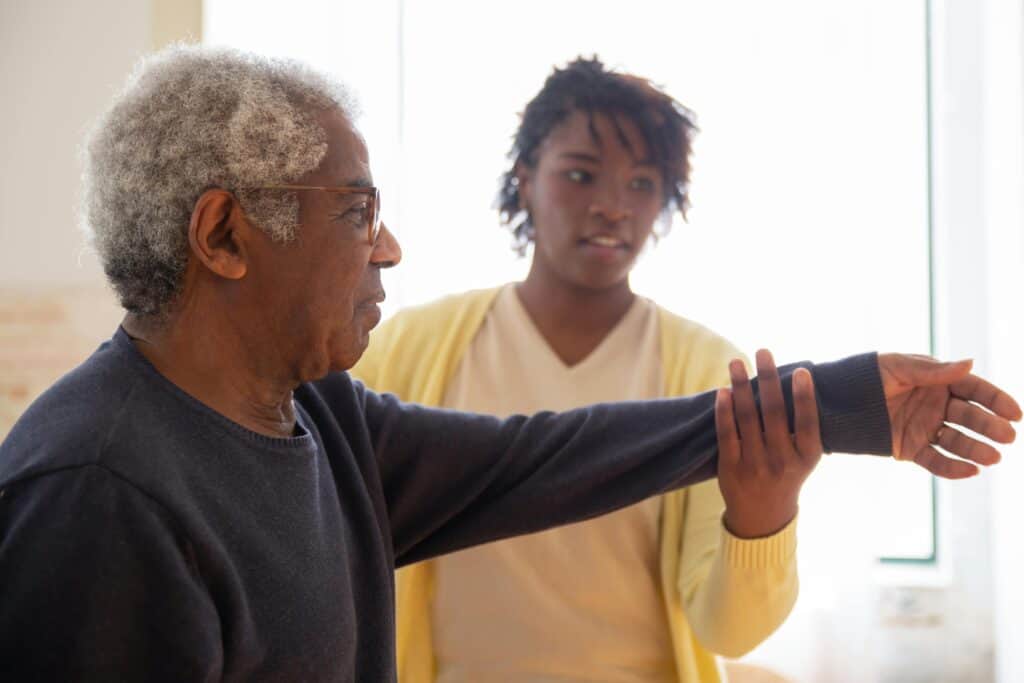 woman helping elderly man stretch arms caregiver