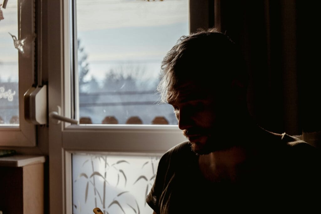 man looking down near window sad