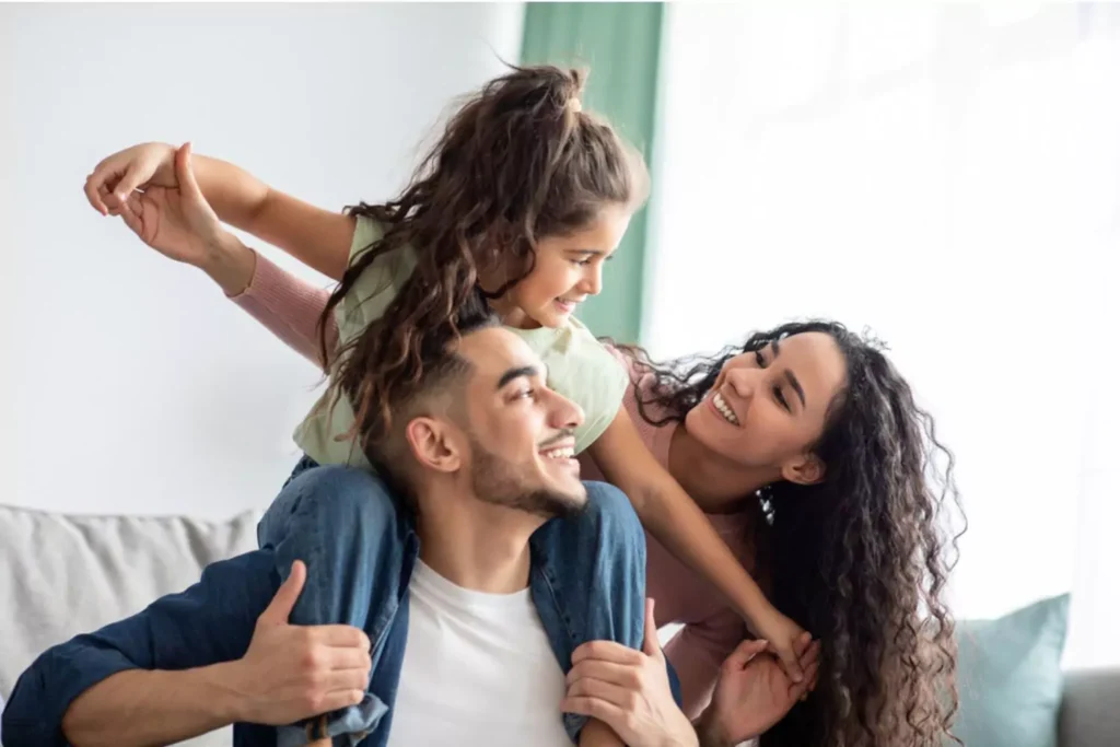 little girl on her daddy's shoulders smiling at her mom