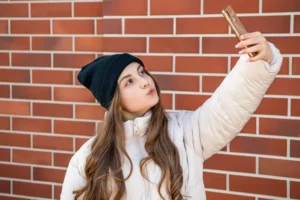 Teen with a smartphone taking a selfie, provoking the question